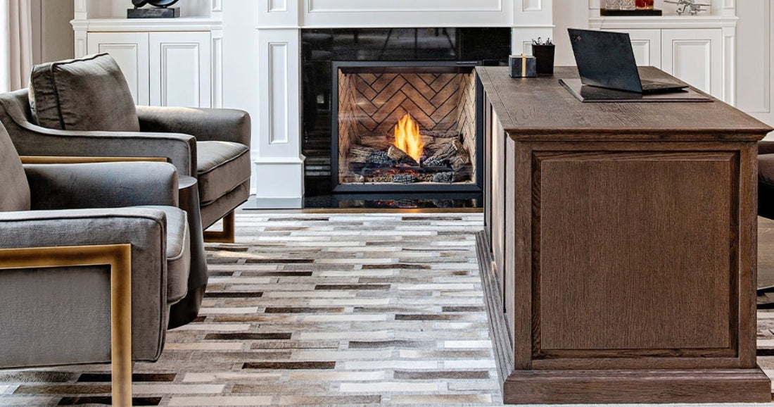 Elegant home office with cozy fireplace, gray armchairs, wooden desk, and stylish patterned rug.