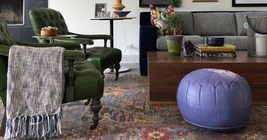 A cozy living room with green armchairs, a colorful area rug, and a purple pouf for decor.