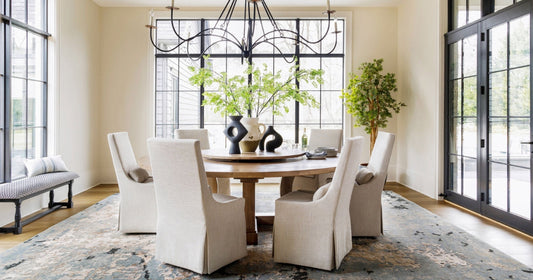 Elegant dining space with a rustic table, neutral chairs, and a textured blue area rug.