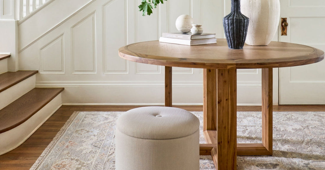 Neutral entryway with a round wood table, decorative vases, and a soft traditional area rug.