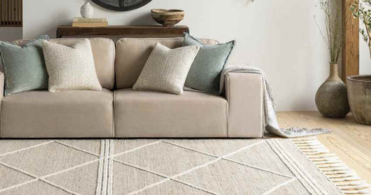 Beige sofa with neutral-toned pillows, styled with a textured tan area rug and earthy decor accents.