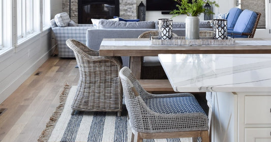 Coastal cottage dining space with wicker chairs, wood table, and navy striped area rug.