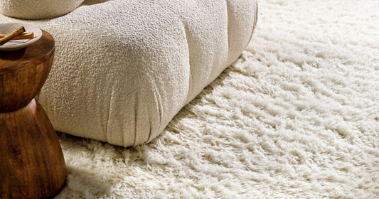 Cream shag rug with a cozy, plush texture next to a wooden stool and textured ottoman.