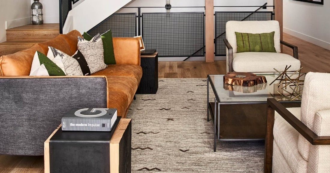 Modern living room with tan leather sofa, neutral armchairs, glass coffee table, and ivory area rug.