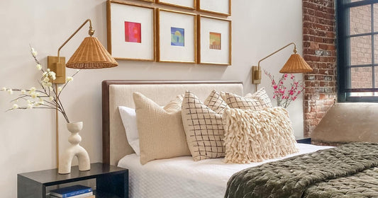 Cozy bedroom with layered pillows, rattan wall sconces, and framed art above a neutral headboard.