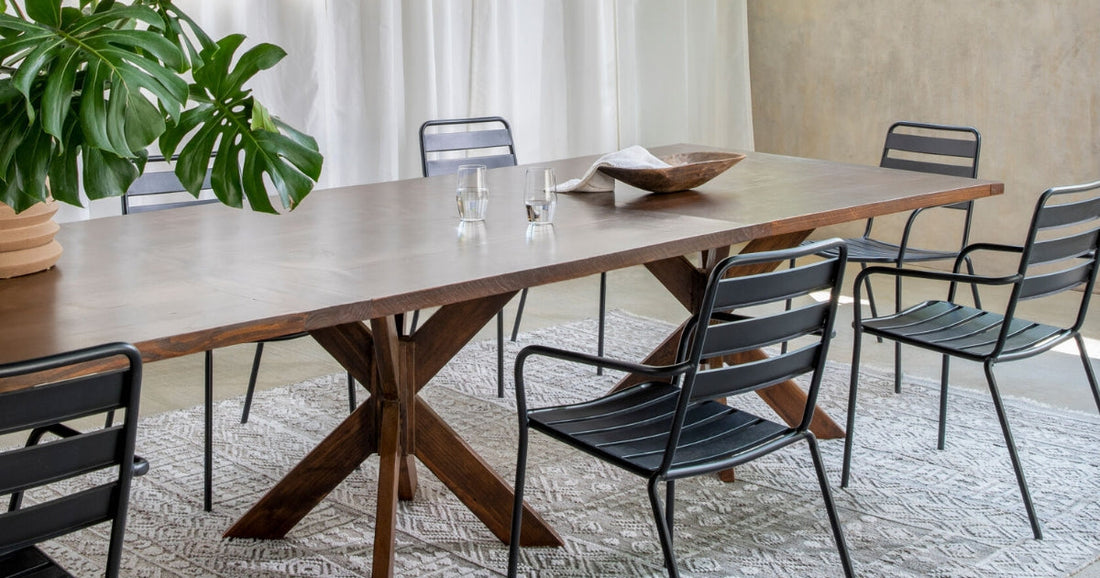 Modern dining room with a wooden table, black metal chairs, a large plant, and a patterned rug.