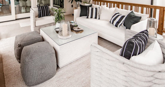 Cozy outdoor seating area with gray poufs, white sofa, striped pillows, and a neutral textured rug.