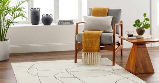 Cozy reading nook with a modern white rug, wooden chair, mustard throw, and greenery.