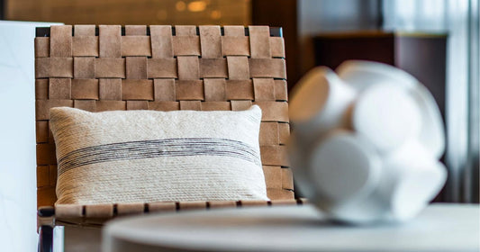 A leather chair with a cream pillow cover featuring black stripes, blurred decor in the foreground.