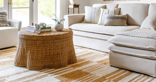 Cozy living room with a neutral sofa, woven coffee table, and a camel tan patterned rug.