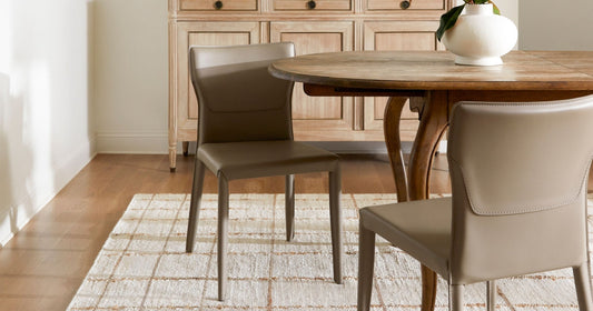 Dining room featuring a rustic wooden table, beige leather chairs, and a textured rug.