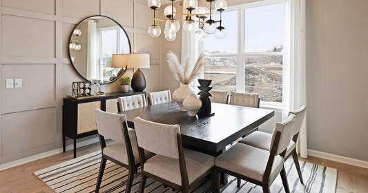 A modern dining room with a round mirror, chic lighting, and a black and white striped area rug.