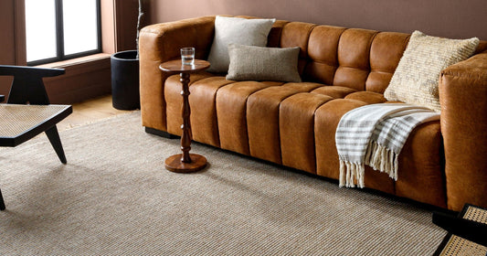 Cozy living room with a tan leather sofa, neutral pillows, and a textured taupe area rug.