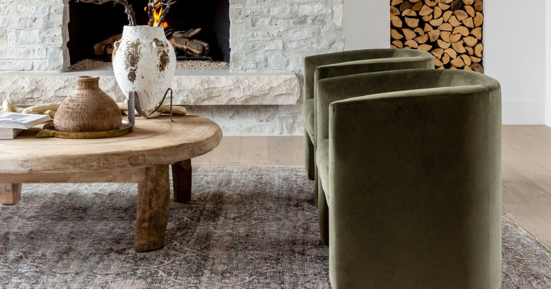 A cozy living room with green velvet chairs, a round rustic wooden coffee table, and a fireplace.