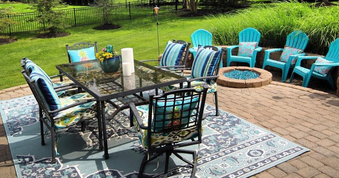 Vibrant outdoor setup featuring a glass dining table, blue chairs, and a traditional aqua area rug.