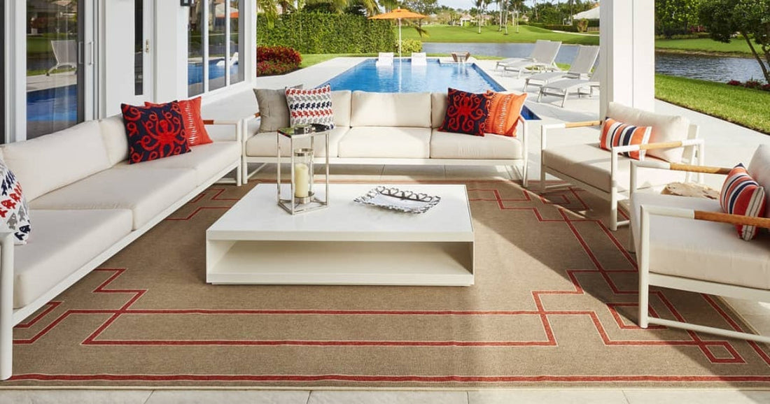 Outdoor seating area with a white sectional, pillows, and a beige rug with red geometric accents.