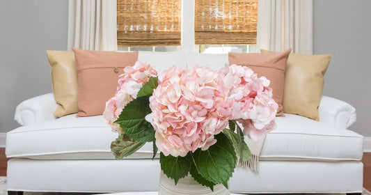 Cozy white sofa with peach pillows and a vase of pink hydrangeas for a fresh, elegant vibe.