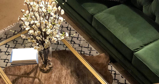 Elegant living room with a green sofa, patterned rug, and floral centerpiece on glass table.