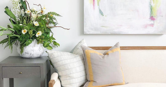 A living space with a neutral sofa, colorful art, and a vibrant floral arrangement on a side table.